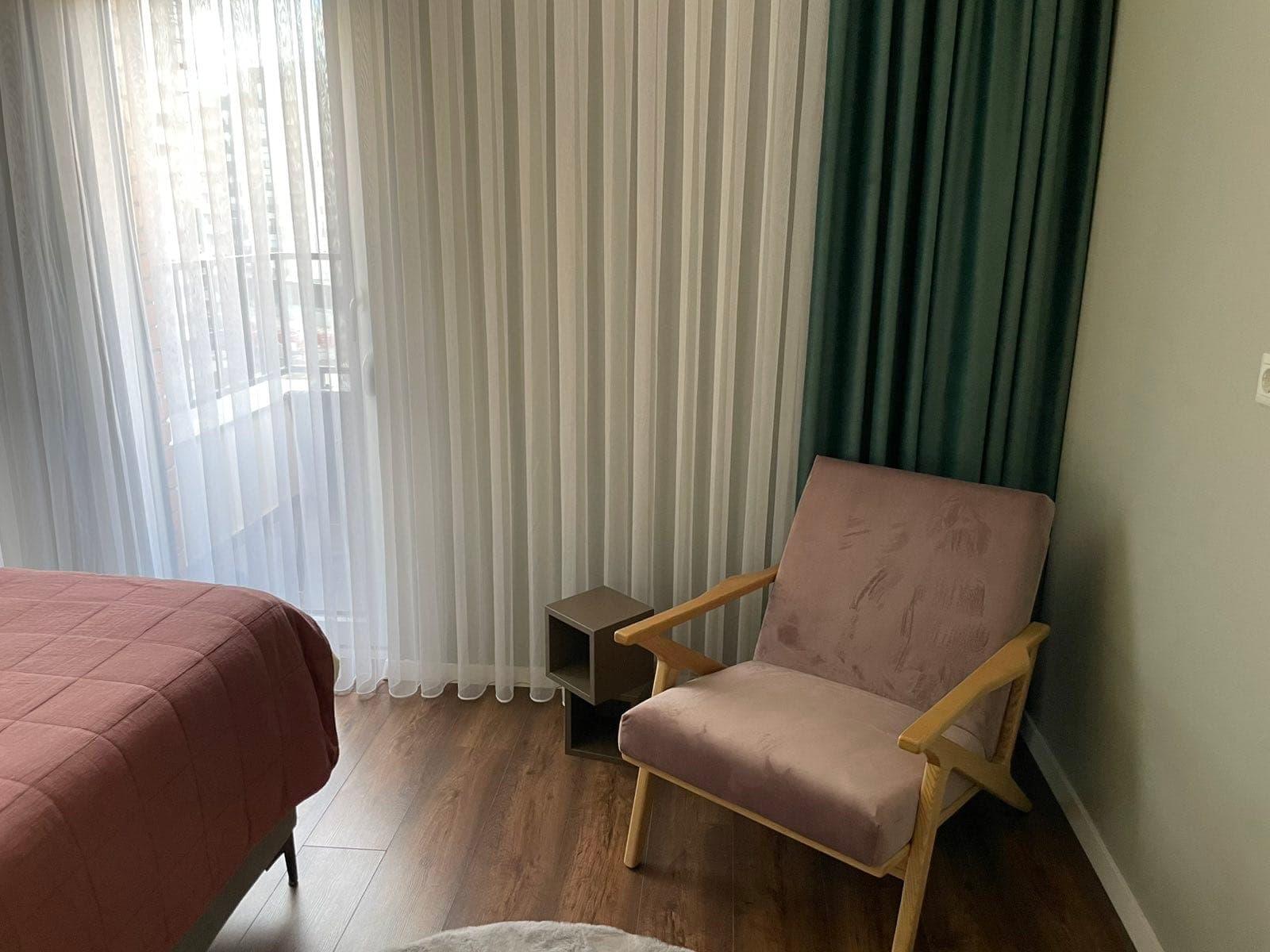 Pink armchair beside sheer curtains in the bedroom