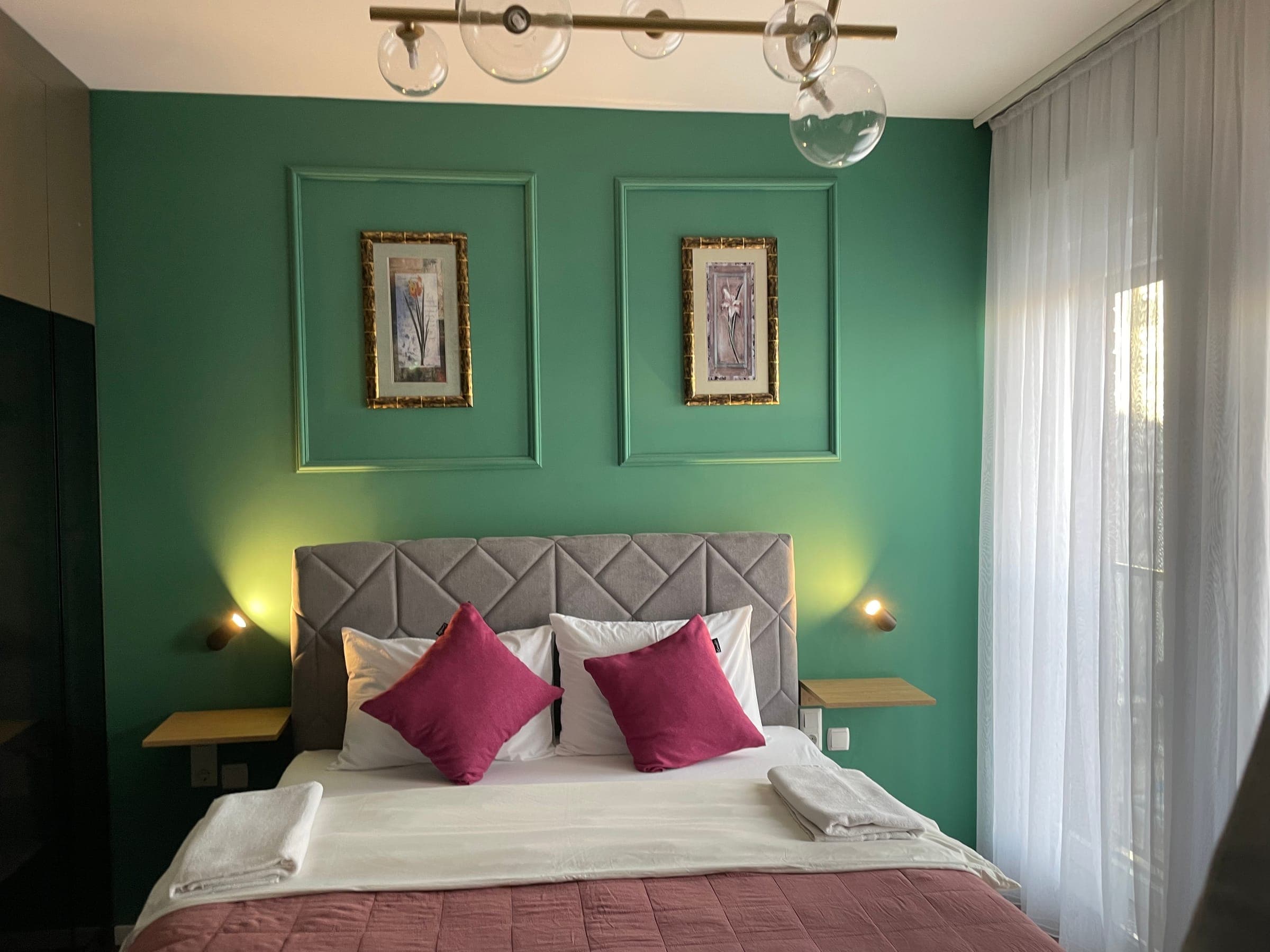 Bedroom with the sage green wall, framed prints and pink cushions