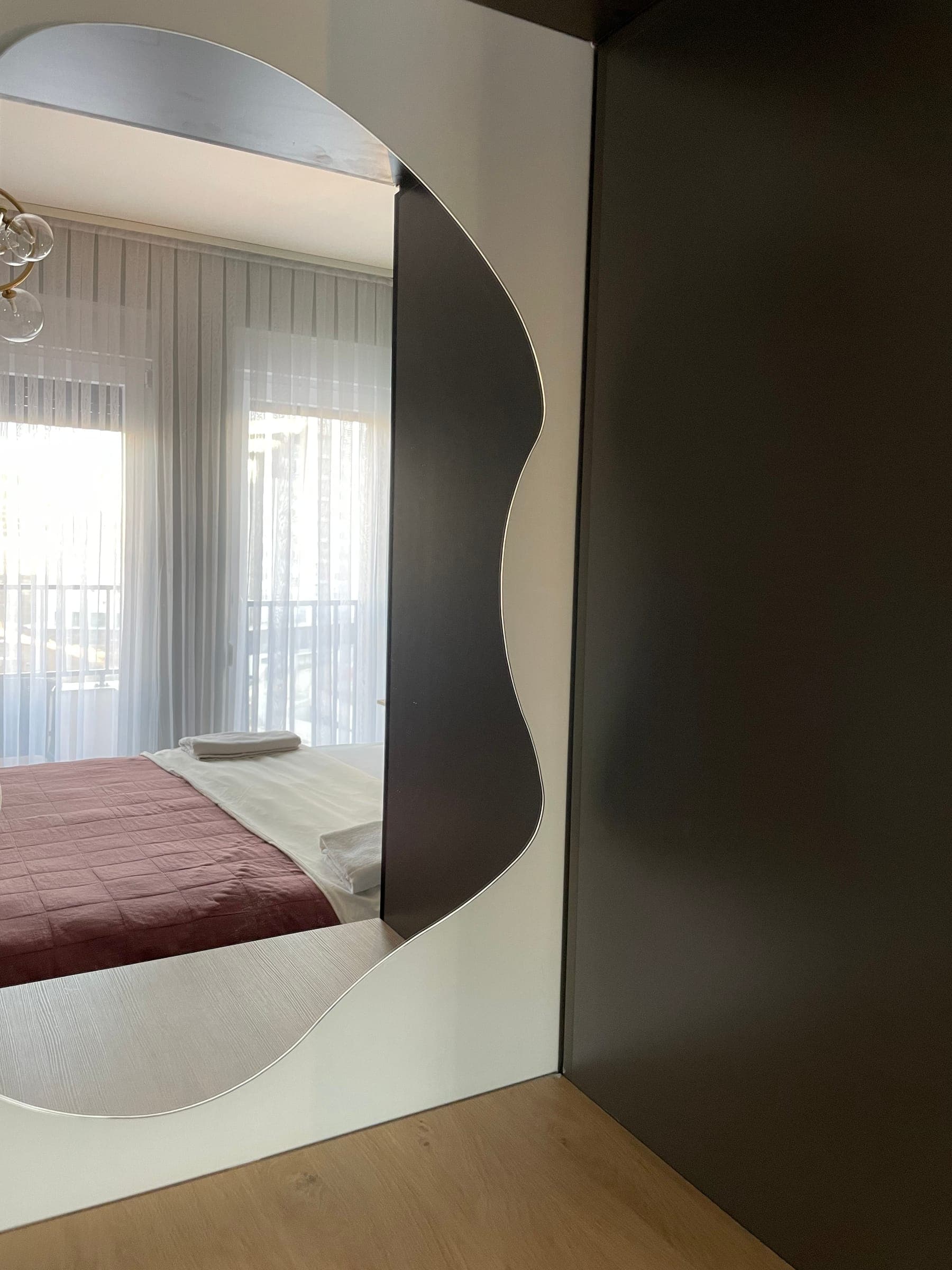 Organic-shaped mirror on the wardrobe reflecting the bedroom