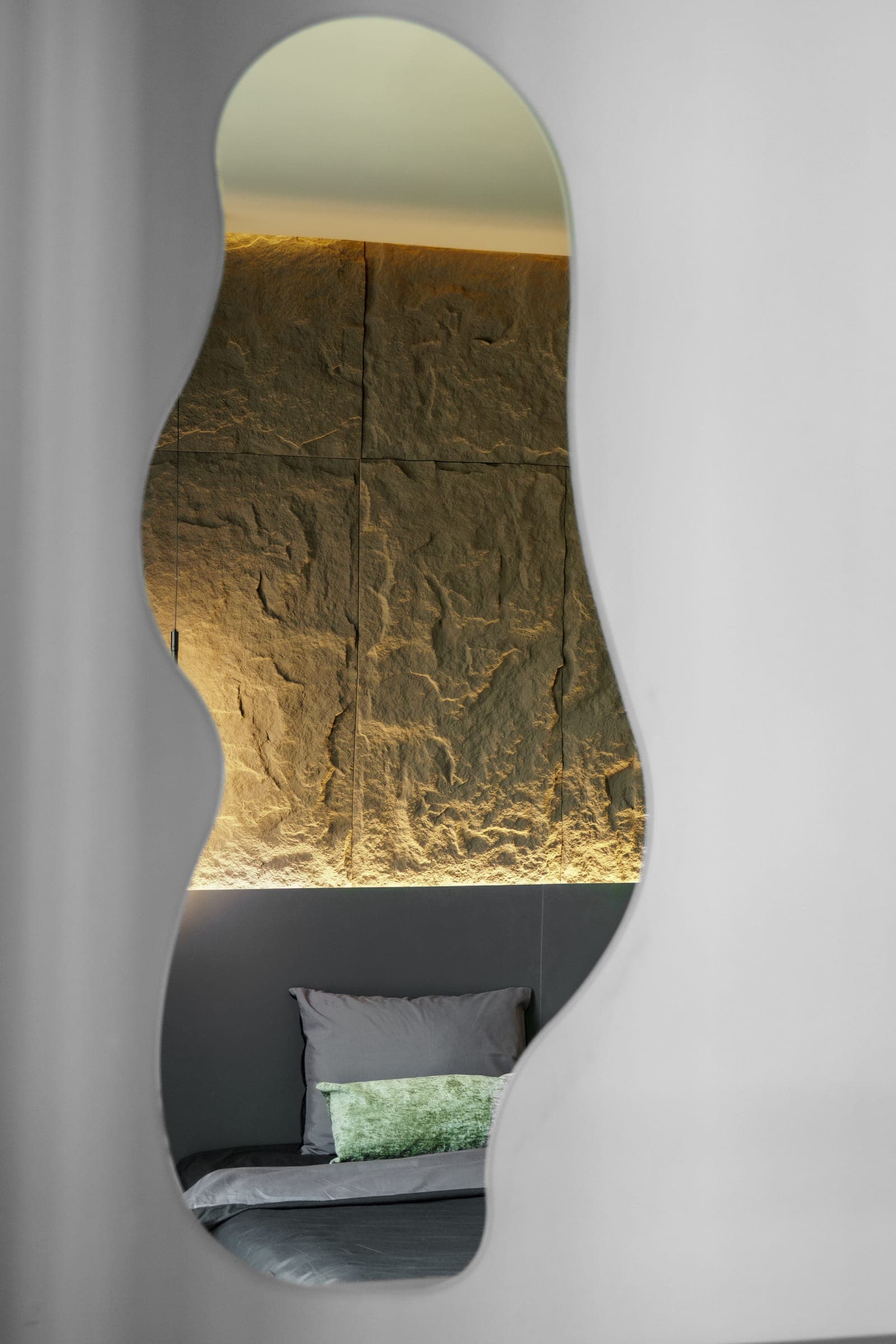 Organic mirror reflecting the textured, softly lit bedroom feature wall